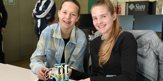 Zwei Schülerinnen posieren mit einem Roboter