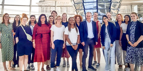 Gruppenfoto: 17 Frauen und ein Mann im Anzug, im Hintergrund: Reichstagskuppel