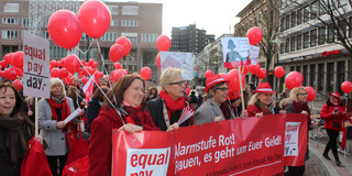 Frauen in rot gekleidet machen mit Ballons und Banner auf ungleiche Bezahlung aufmerksam